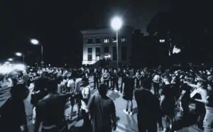 A large crowd gathers at night outside a building during a political rally as police stand in formation facing the protesters